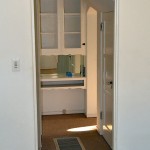 A door leads out of the den into a hall with a door to the basement on the right and a small desk area ahead..